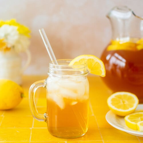 mason jar glass of homemade sweetened iced tea on a yellow tile table.