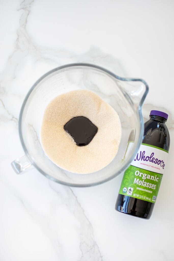 cane sugar and molasses in a glass mixing bowl on a white marble counter.