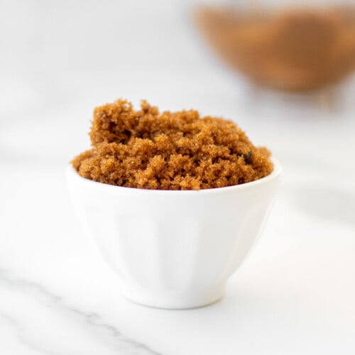 homemade light brown sugar in a small white bowl on a marble counter.