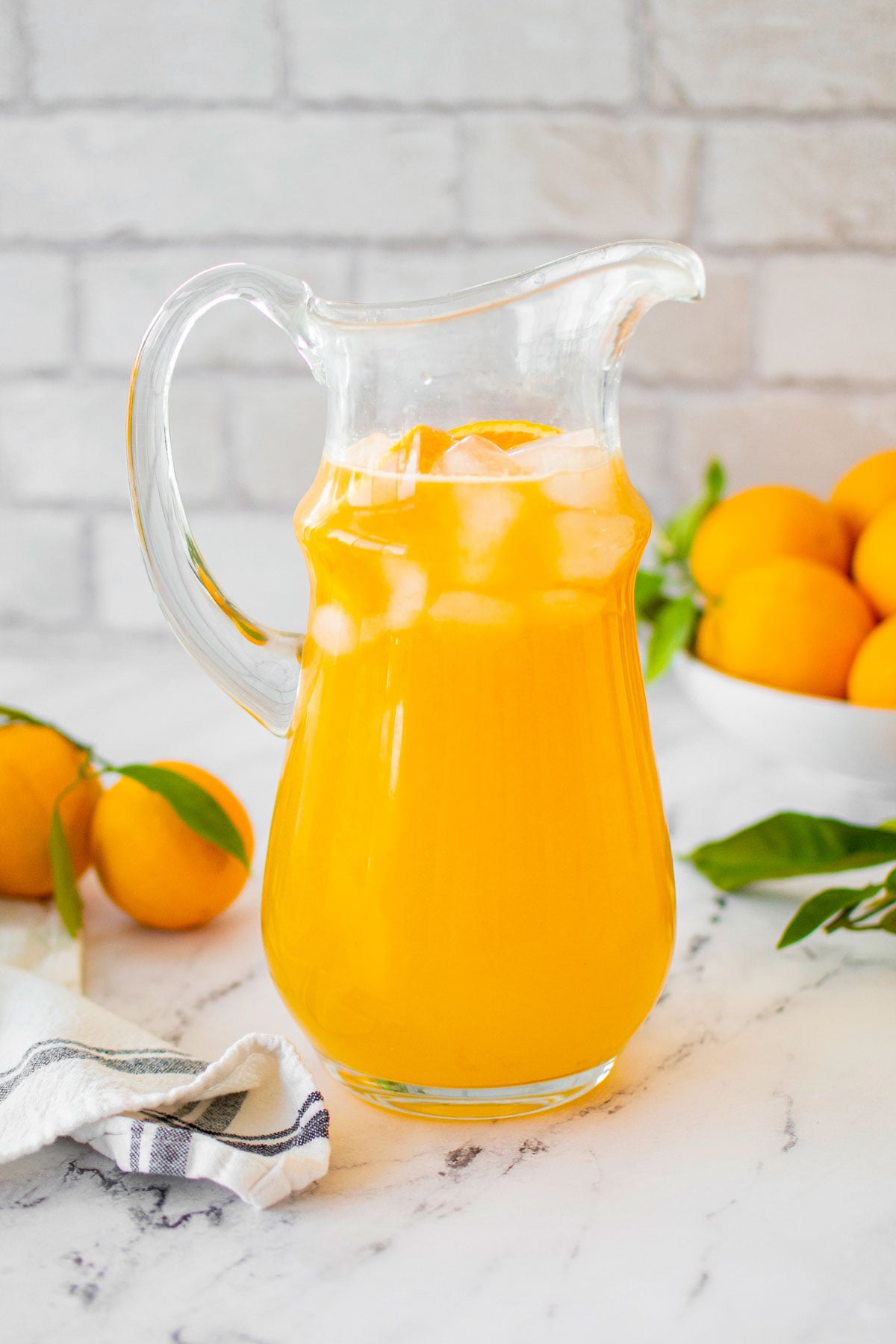 homemade orangeade in a glass pitcher on a white marble counter with fresh oranges.