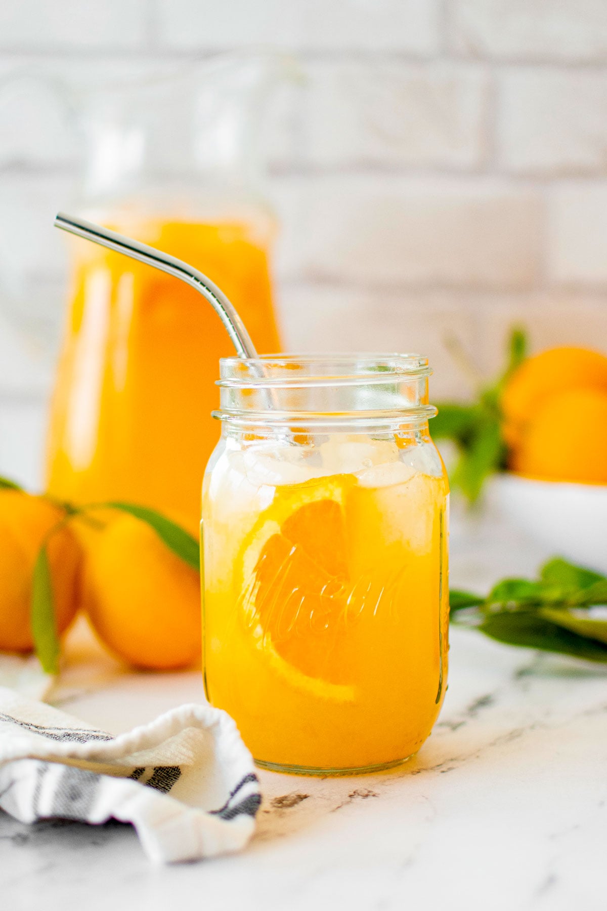 homemade orangeade in a mason jar on a marble countertop with fresh oranges.