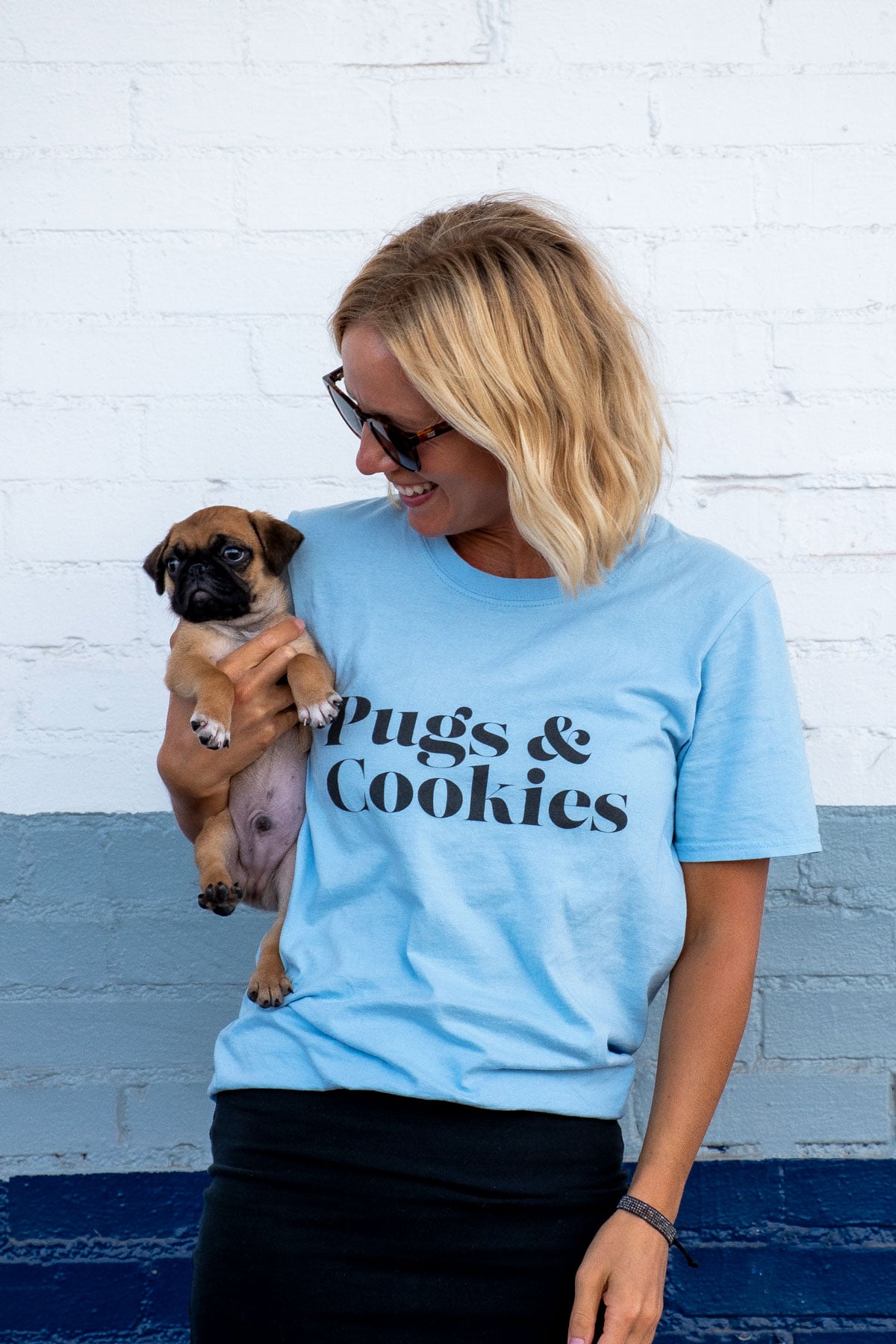 woman holding a pug puppy wearing a pugs and cookies tee shirt.