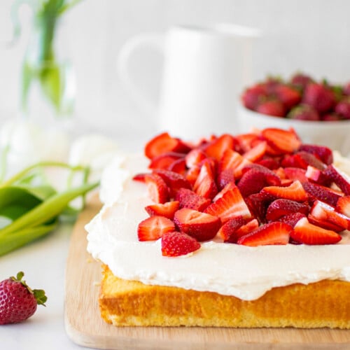 organic strawberry shortcake with homemade whipped cream and fresh strawberries on a wood serving board on a marble table.