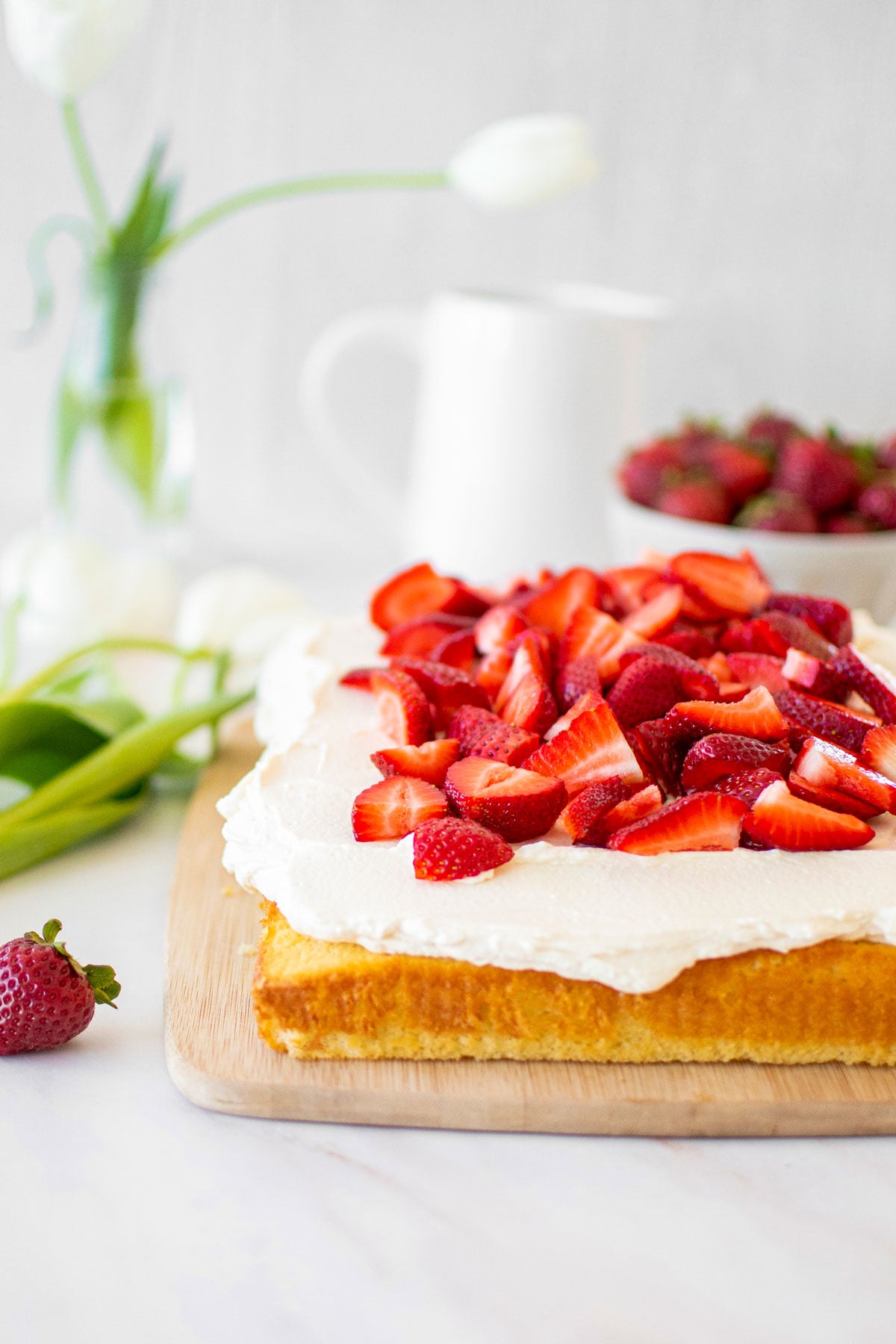 organic strawberry shortcake with homemade whipped cream and fresh strawberries on a wood serving board on a marble table.