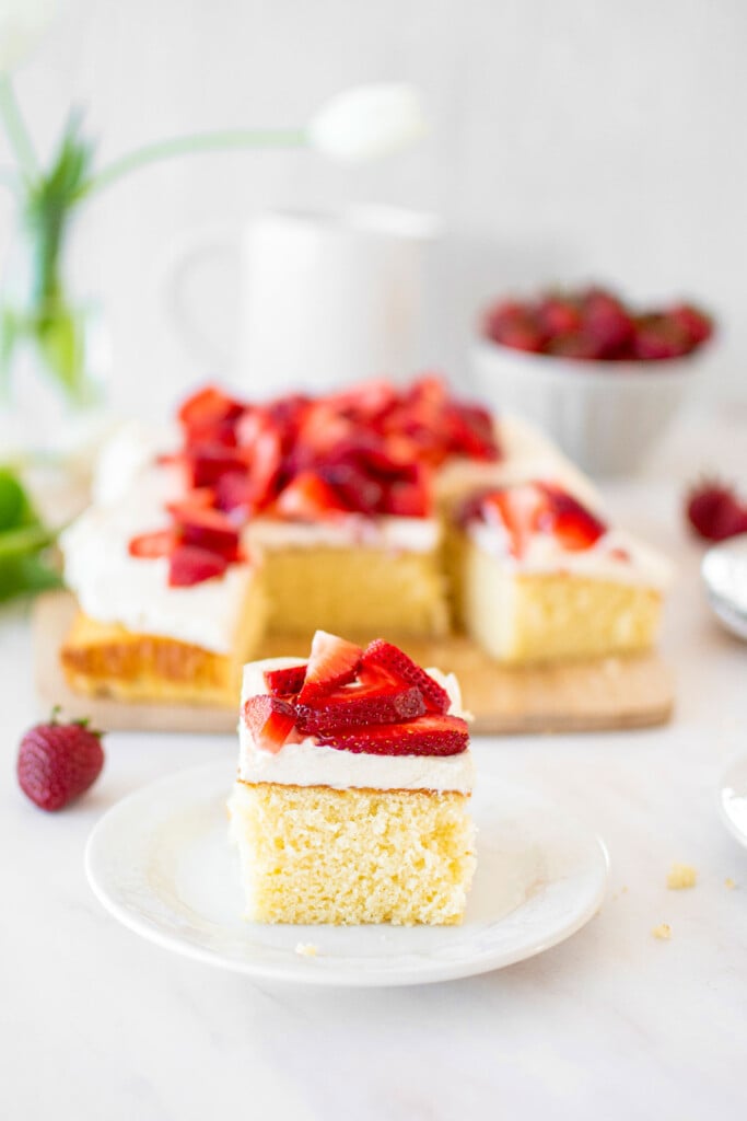 slice of organic strawberry shortcake on a cake plate with fresh strawberries on a marble table.