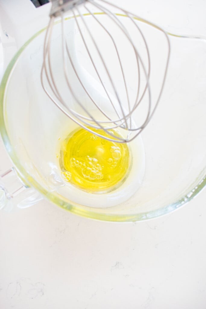 glass mixing bowl with egg whites on a white marble counter.