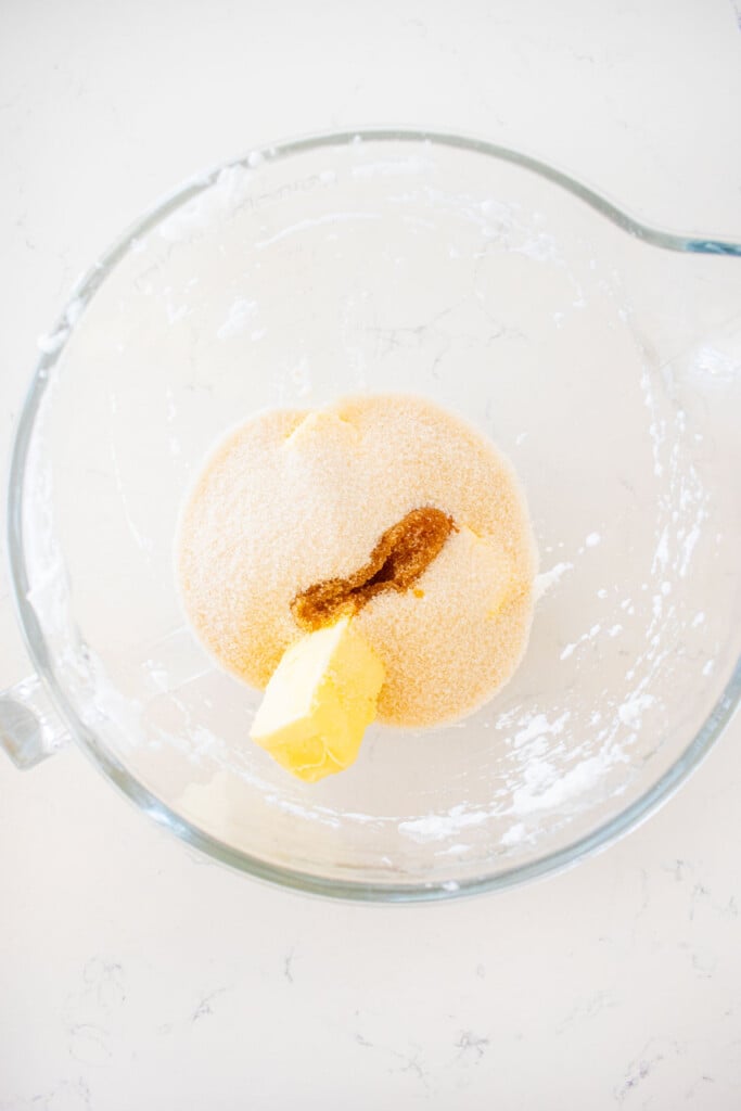 glass mixing bowl with butter, cane sugar and vanilla on a white marble counter.