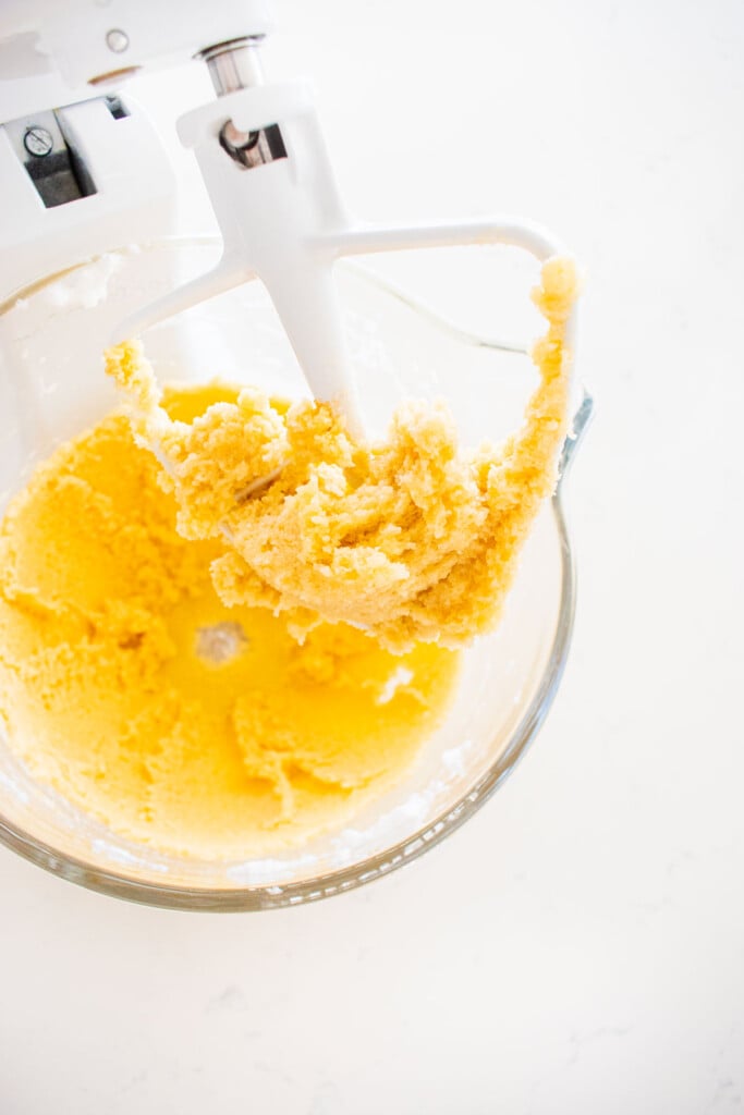creamed butter and sugar in a glass stand mixing bowl on a white marble counter.