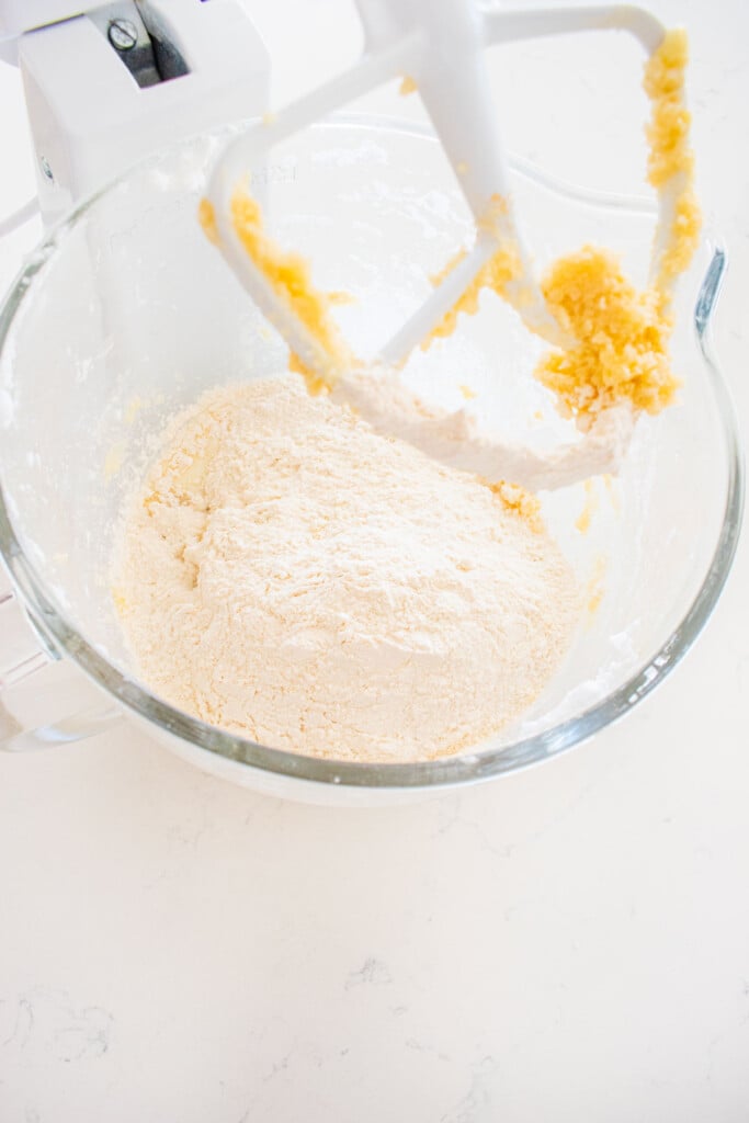 ingredients for white cake in a glass stand mixing bowl on a white marble counter.