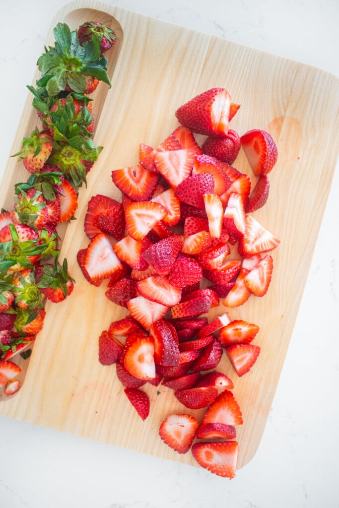 sliced strawberries on a wood cutting board.