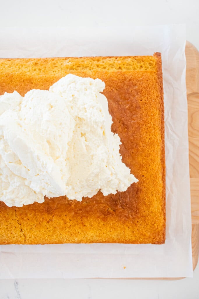 white cake with whipped cream being added on top on a white marble counter.