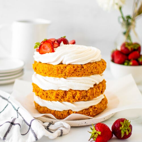 vegan strawberry carrot cake on a cake plate with fresh strawberries on a table with fresh flowers.