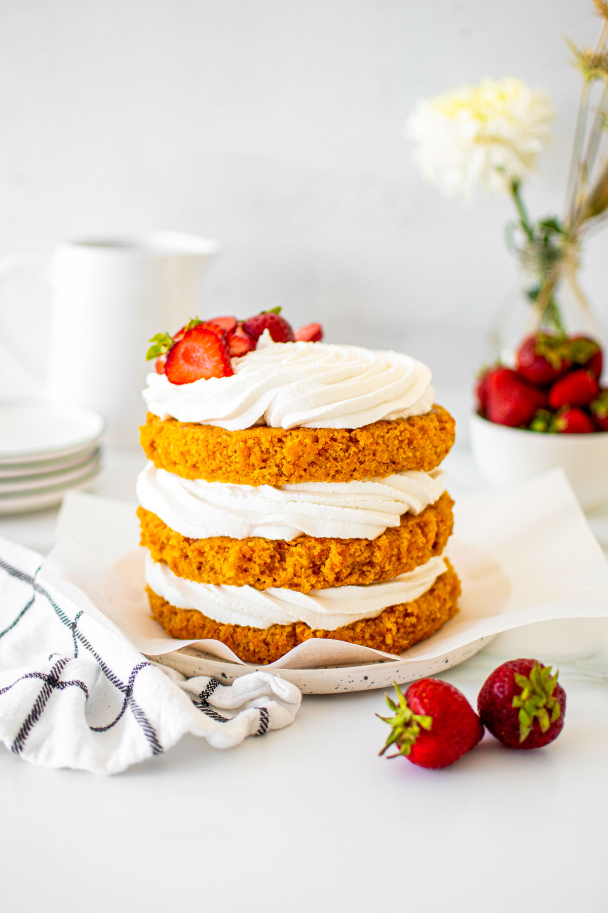 vegan strawberry carrot cake on a cake plate with fresh strawberries on a table with fresh flowers.