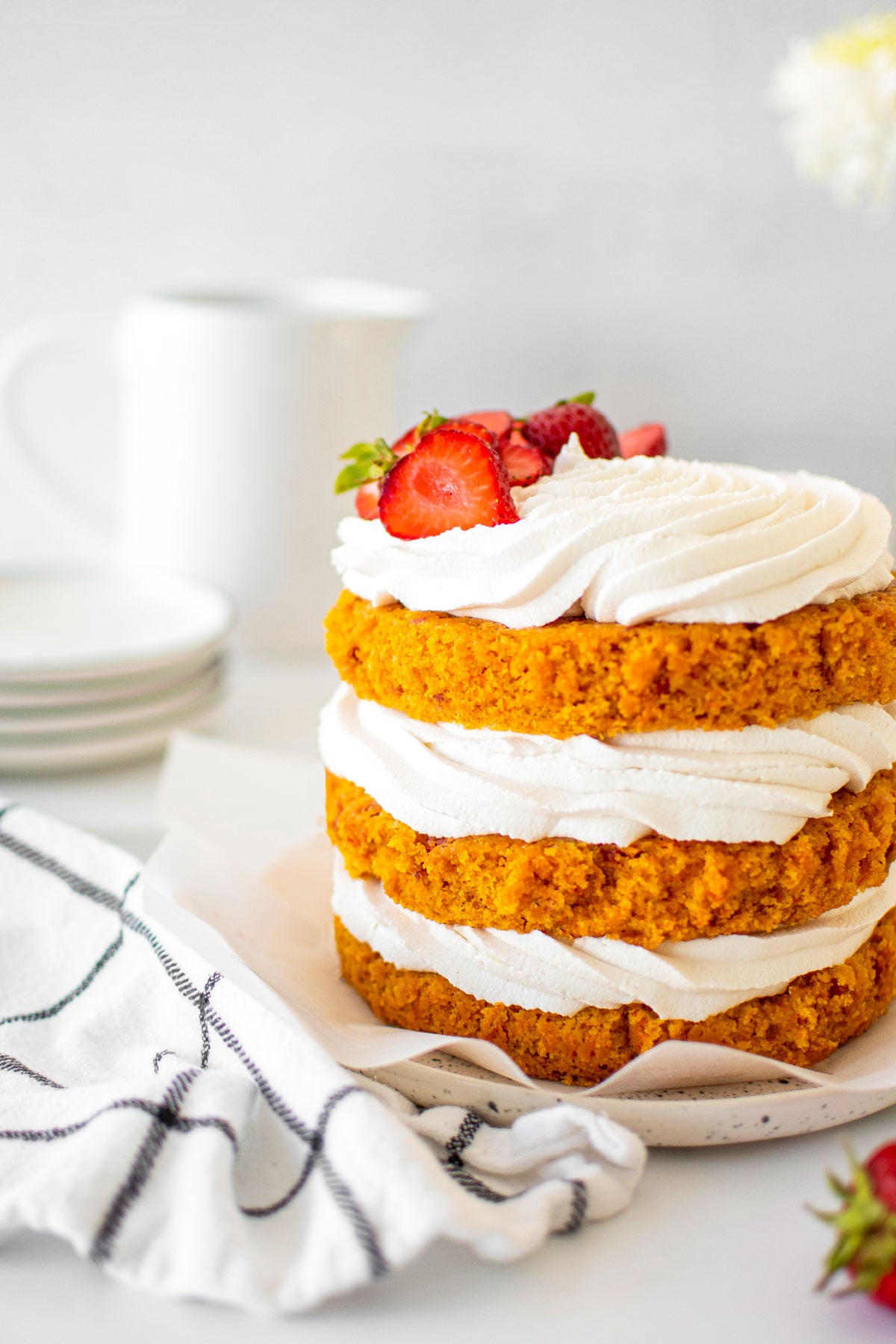 vegan strawberry carrot cake on a cake plate with fresh strawberries on a table with fresh flowers.