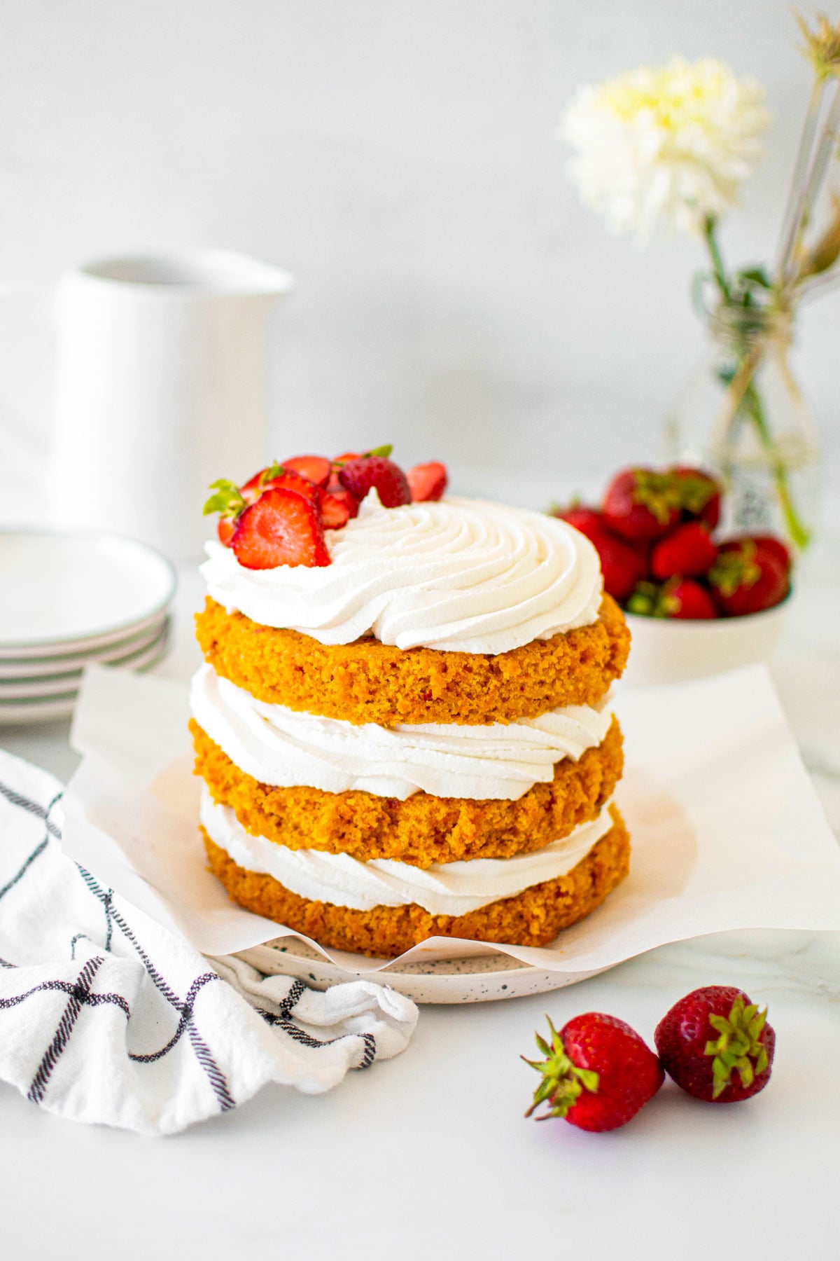 vegan strawberry carrot cake on a cake plate with fresh strawberries on a table with fresh flowers.