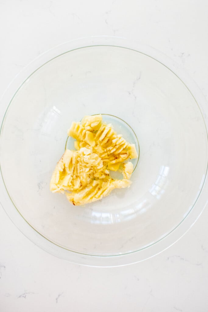 mashed up banana in a glass mixing bowl on a white marble counter.