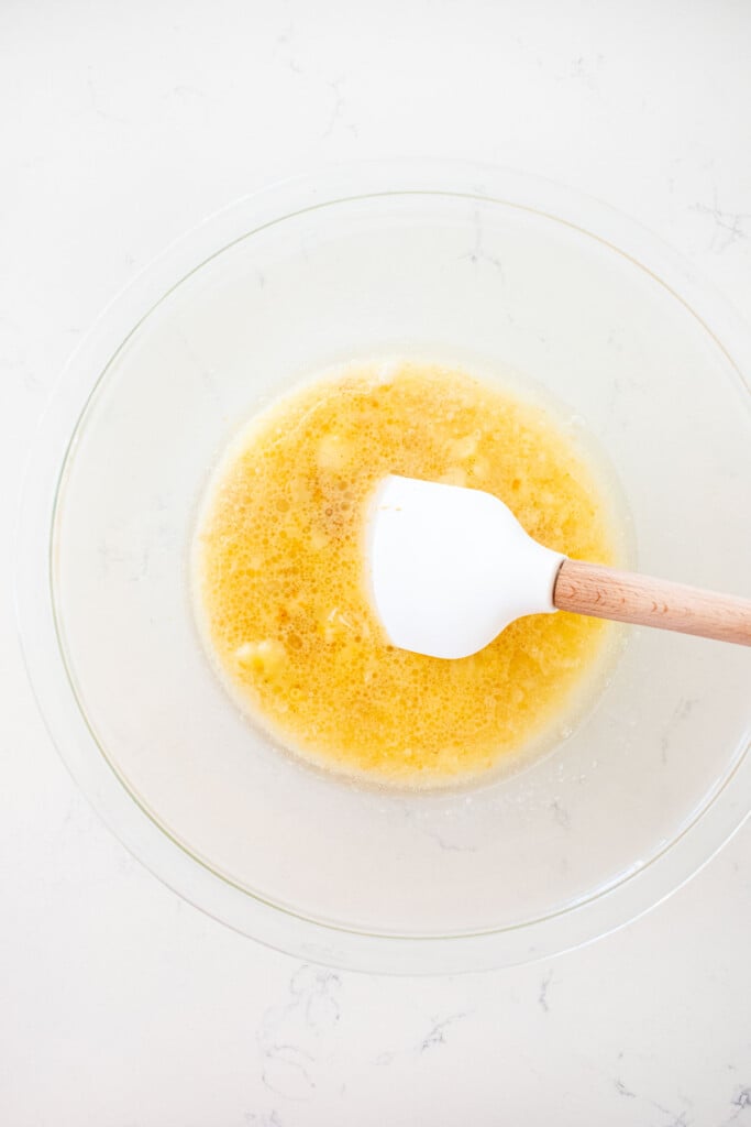 wet ingredients mixed together with a spatula in a glass mixing bowl on a white marble counte.r