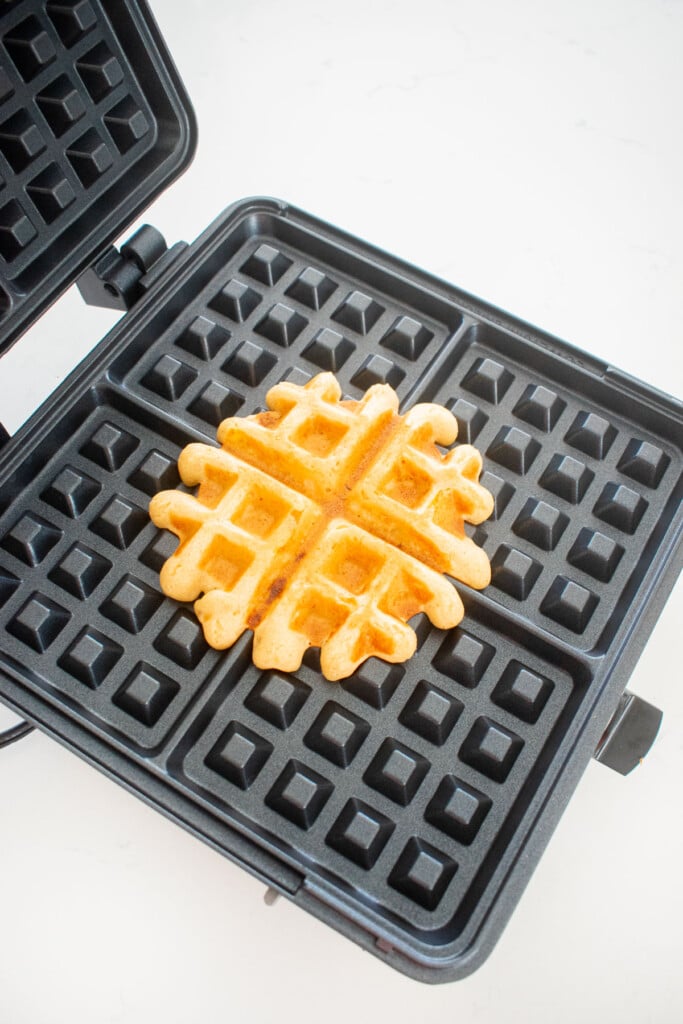 cooked dog waffle in a waffle iron on a white marble counter.