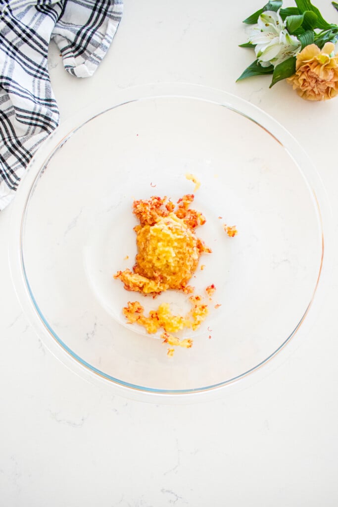 glass mixing bowl with finely grated apple on a marble counter with fresh flowers and a kitchen towel.