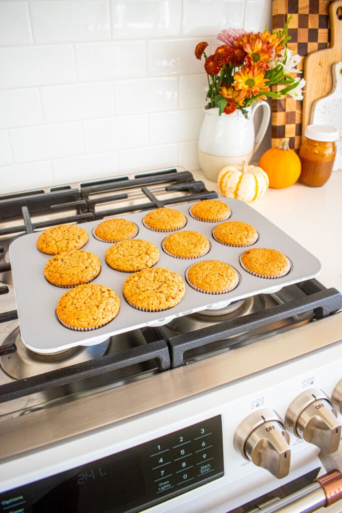 baked apple cinnamon cupcakes in a cupcake pan cooling on top of an oven.