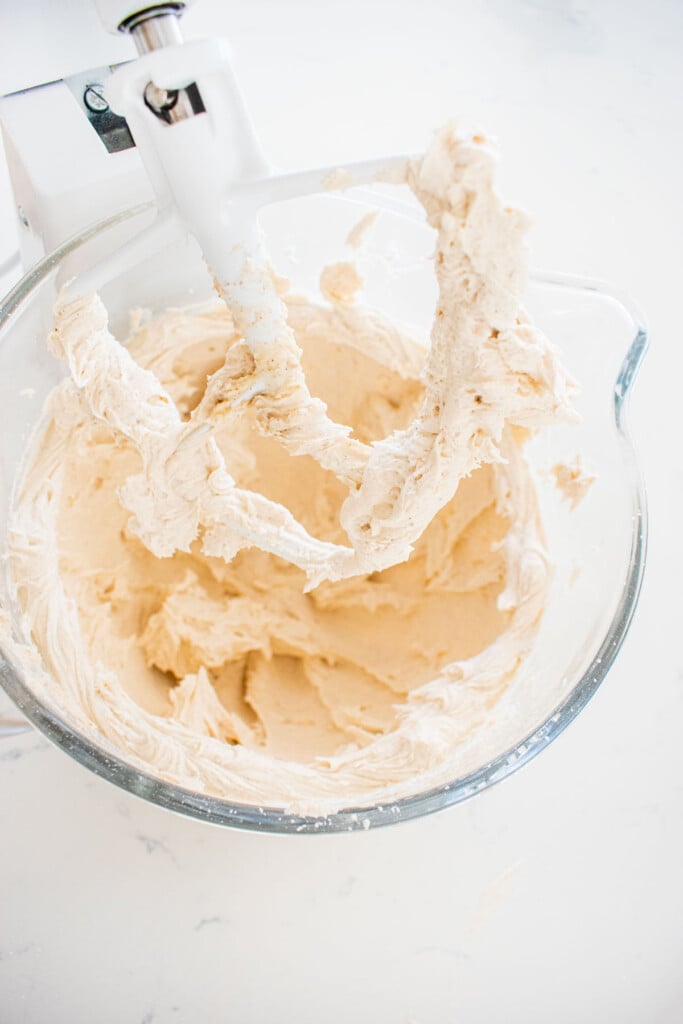 fluffy vanilla bean buttercream frosting in a glass mixing bowl on a marble counter.