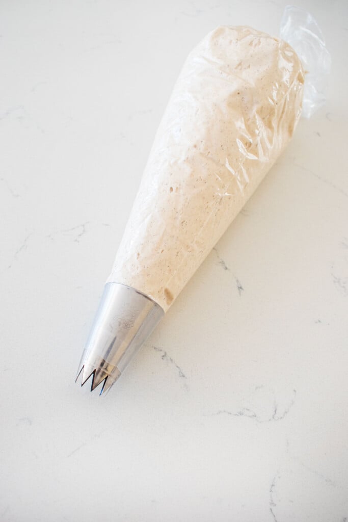 vanilla bean buttercream frosting in a piping bag with an open star tip on a marble counter.