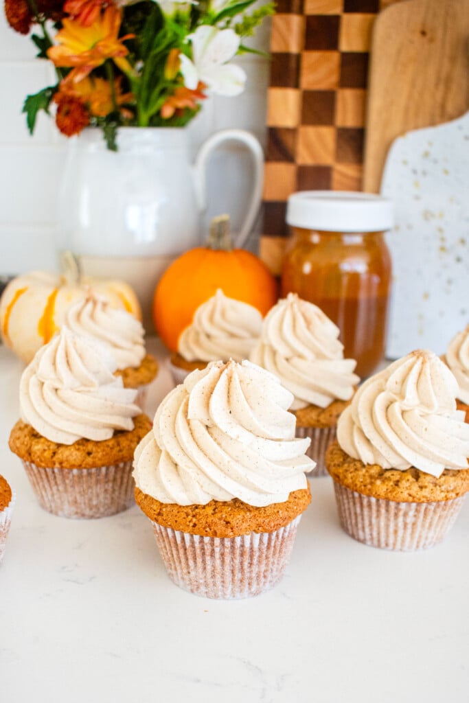 apple cinnamon cupcakes on a marble counter with mini pumpkins and fresh flowers.