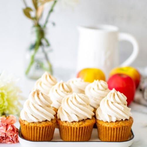 apple cinnamon cupcakes on a white plate on a marble counter with fresh flowers and apples.