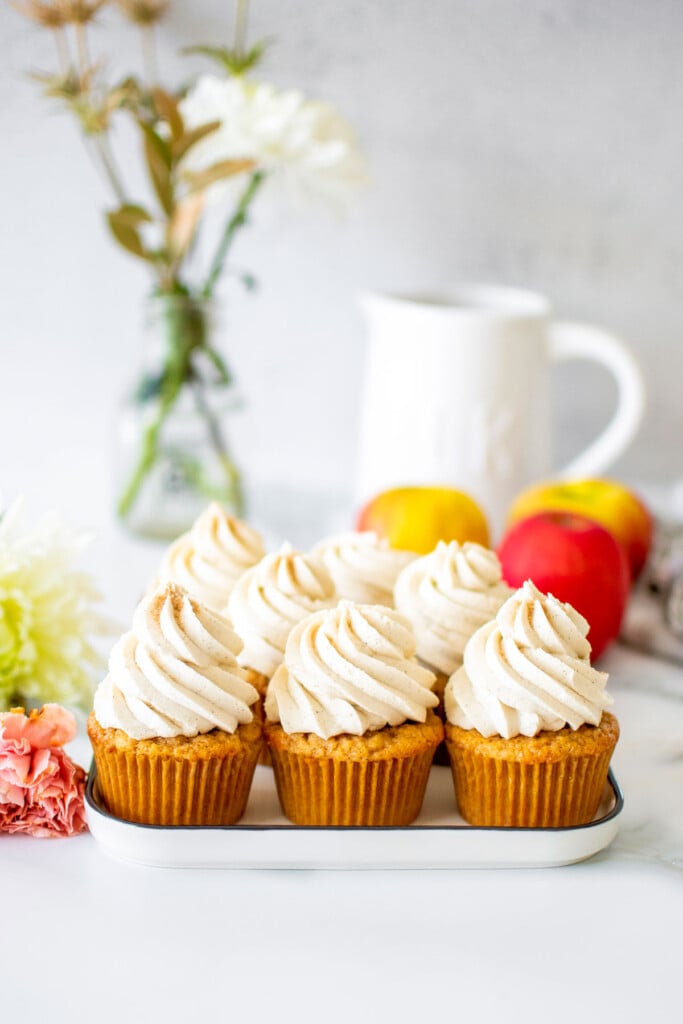 apple cinnamon cupcakes on a white plate on a marble counter with fresh flowers and apples.