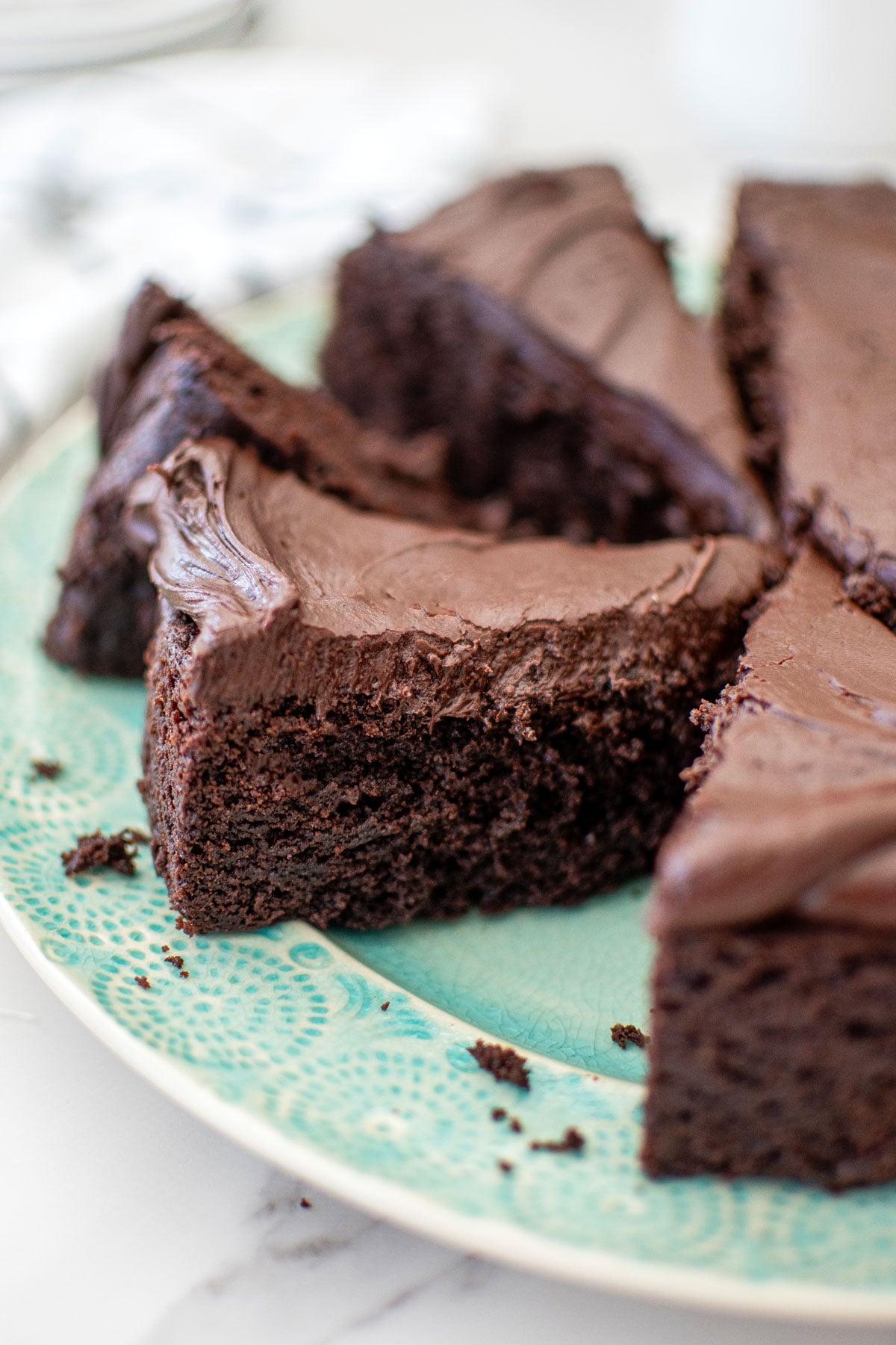 avocado oil chocolate cake cut into slices on a green plate on a white marble countertop.