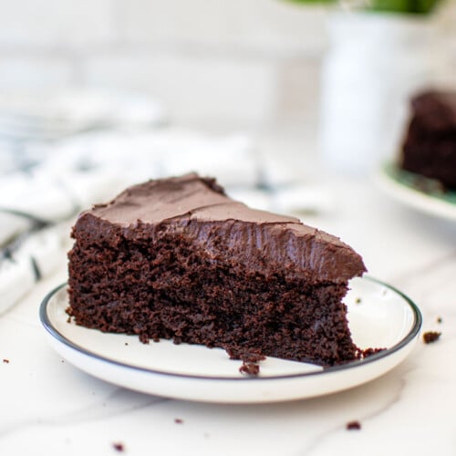 slice of avocado oil chocolate cake on a plate on a white marble countertop.