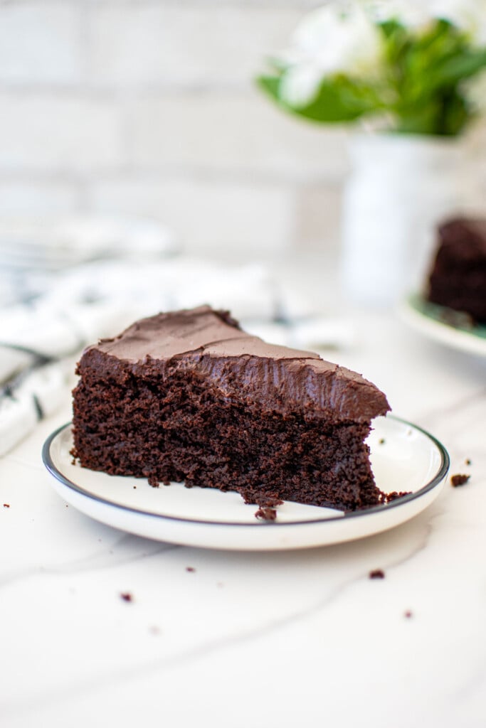 slice of avocado oil chocolate cake on a plate on a white marble countertop.