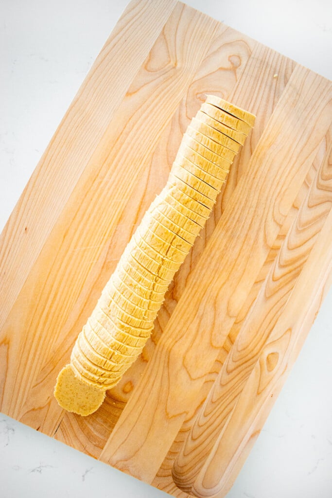 brown sugar shortbread cookie dough log on a wood cutting board sliced into slices.