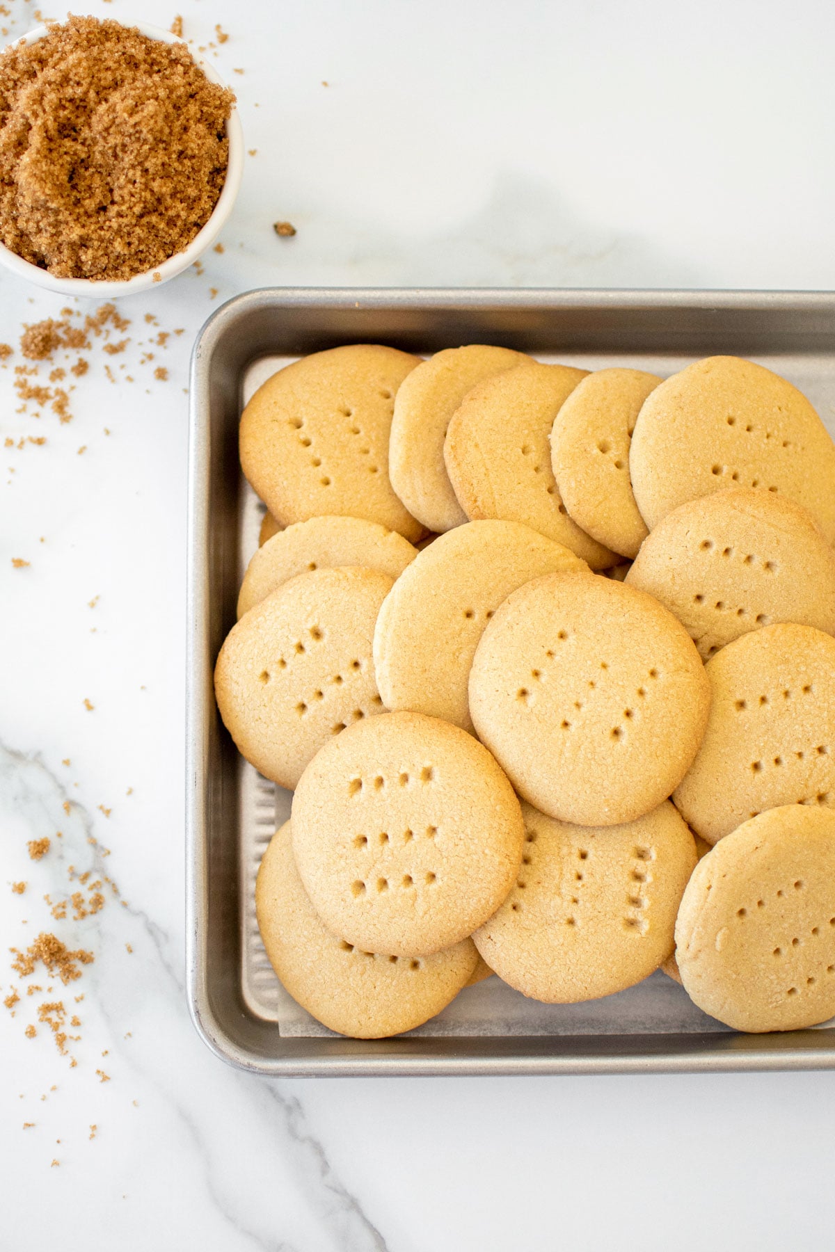 brown sugar shortbread cookies on a baking sheet on a white marble counter.