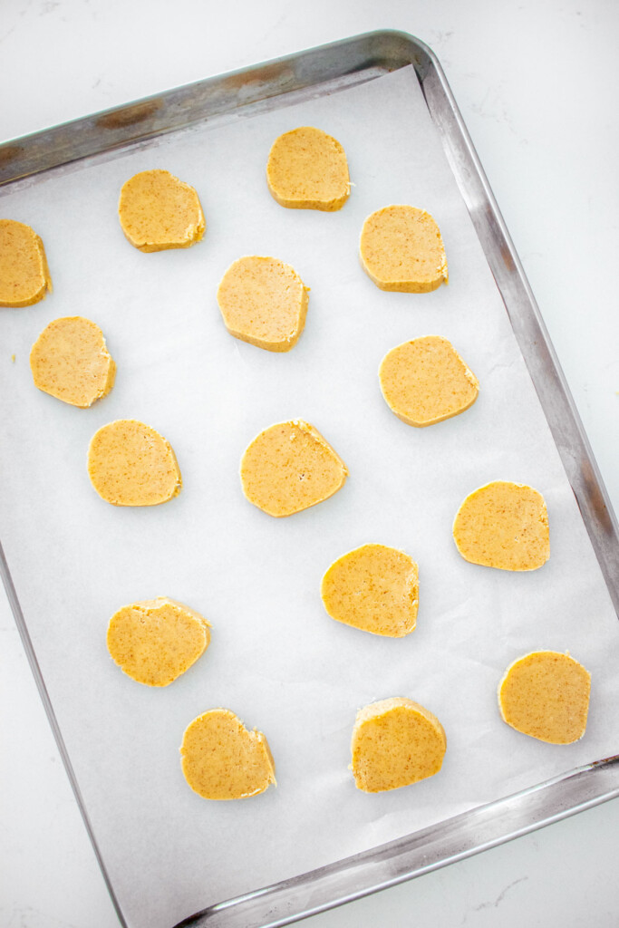 baking sheet with brown sugar shortbread cookie slices spread out evenly on a white marble counter.