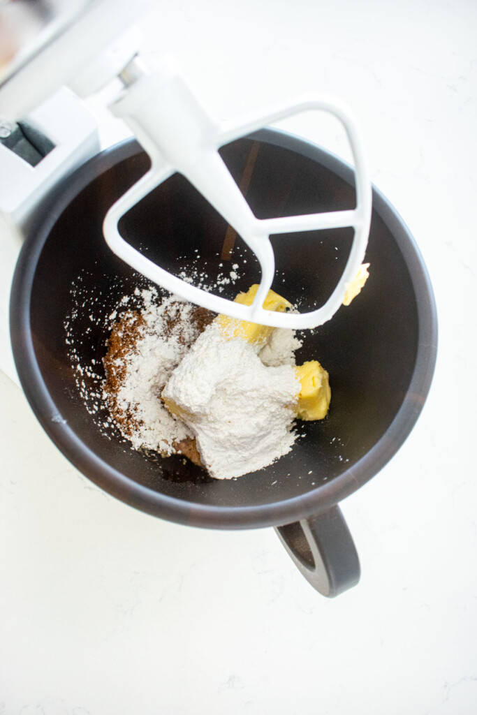 wood baking bowl with butter, brown sugar and powdered sugar on a white marble counter.