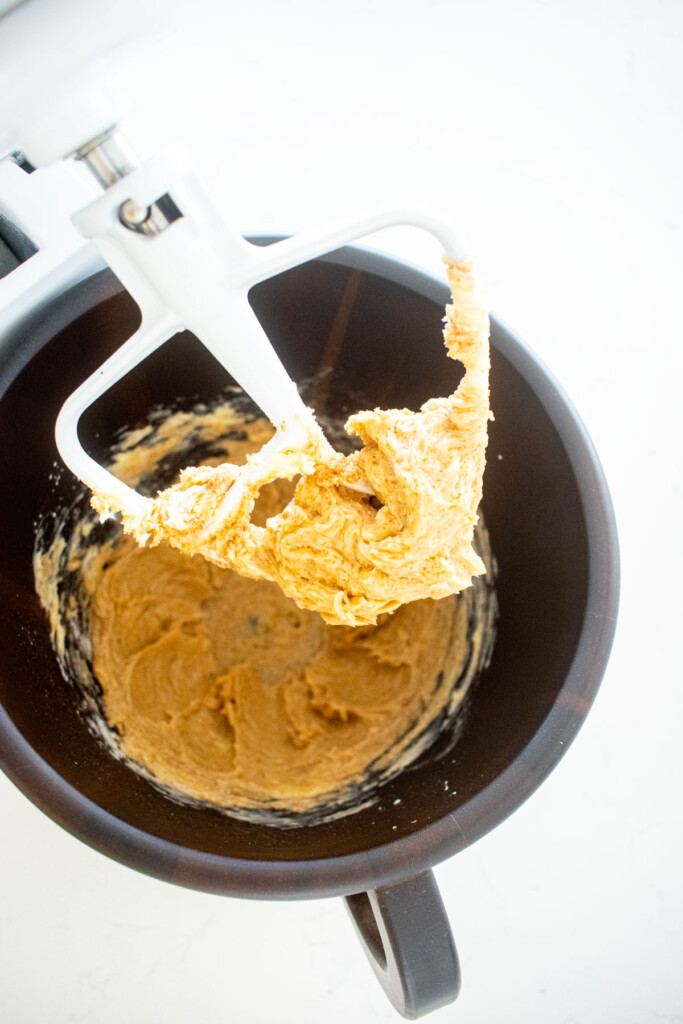 wood baking bowl with creamed butter, brown sugar and powdered sugar on a white marble counter.