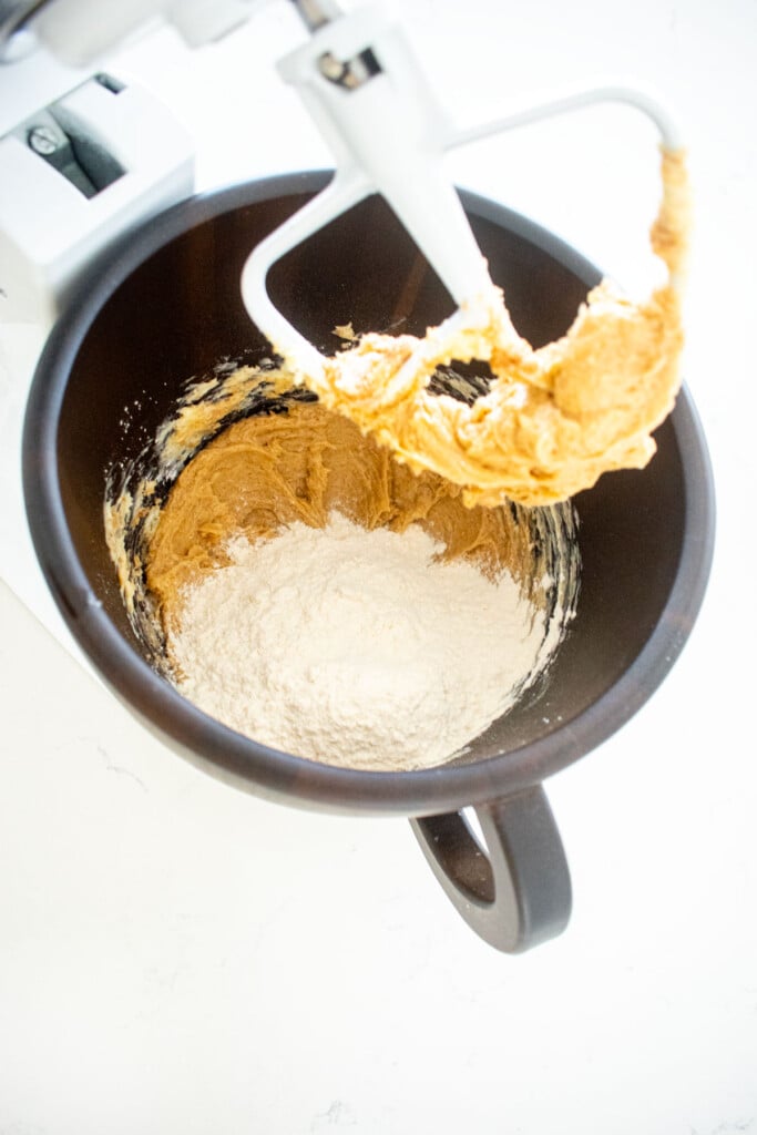 flour added to creamed butter and sugar in a wood mixing bowl on a white marble counter.