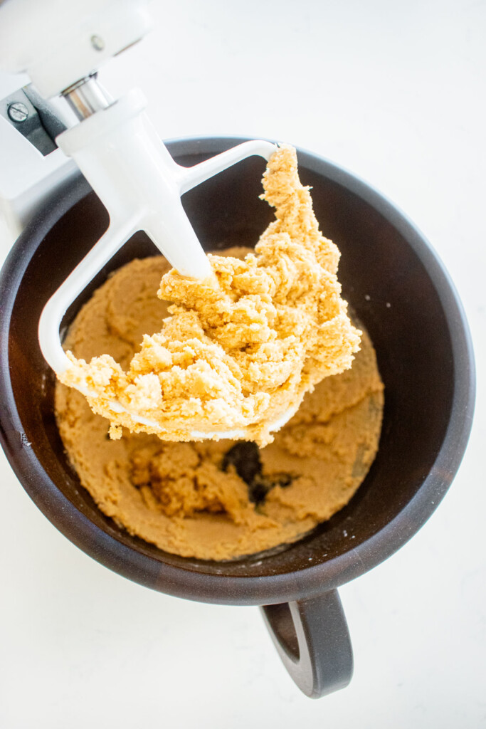 brown sugar shortbread cookie dough in a wood mixing bowl on a white marble counter.