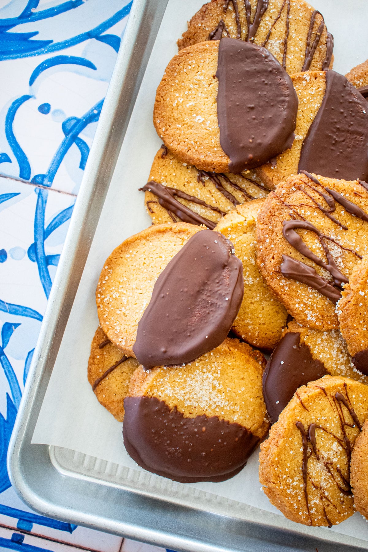 brown sugar shortbread cookies, some half dipped in chocolate on a baking sheet on a blue tile table.