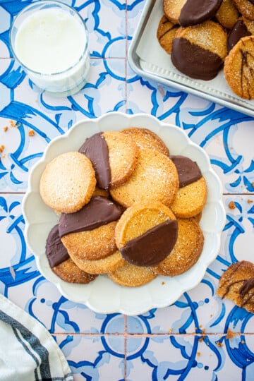 brown sugar shortbread cookies on a plate on a blue tile table with a glass of milk.