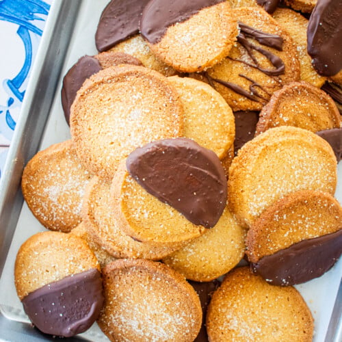 brown sugar shortbread cookies, some half dipped in chocolate on a baking sheet on a blue tile table.