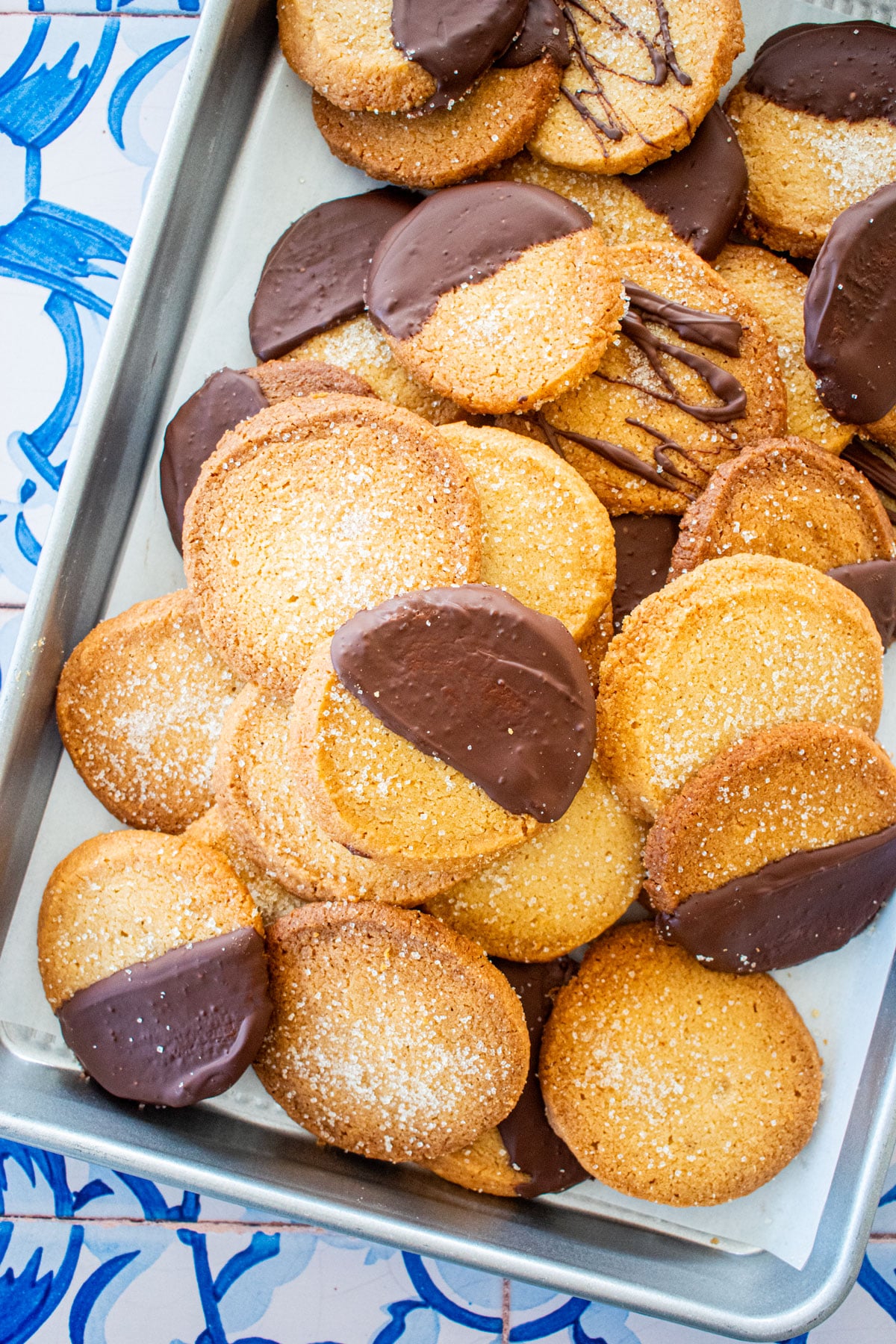 brown sugar shortbread cookies, some half dipped in chocolate on a baking sheet on a blue tile table.