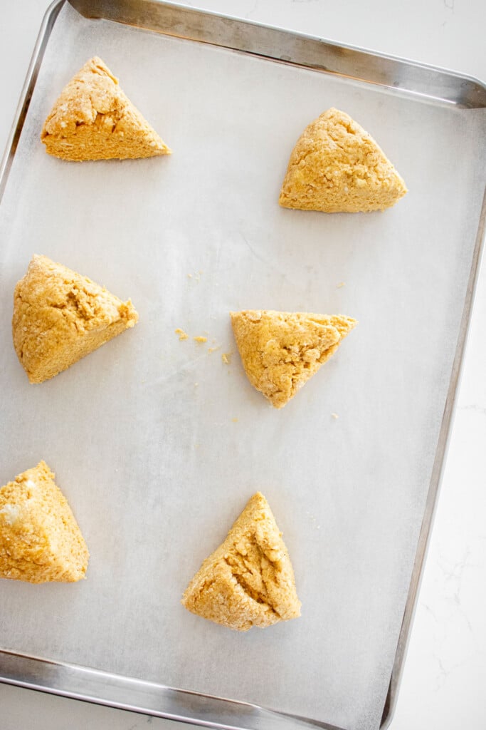raw eggless pumpkin scones on a baking sheet on a white marble counter.