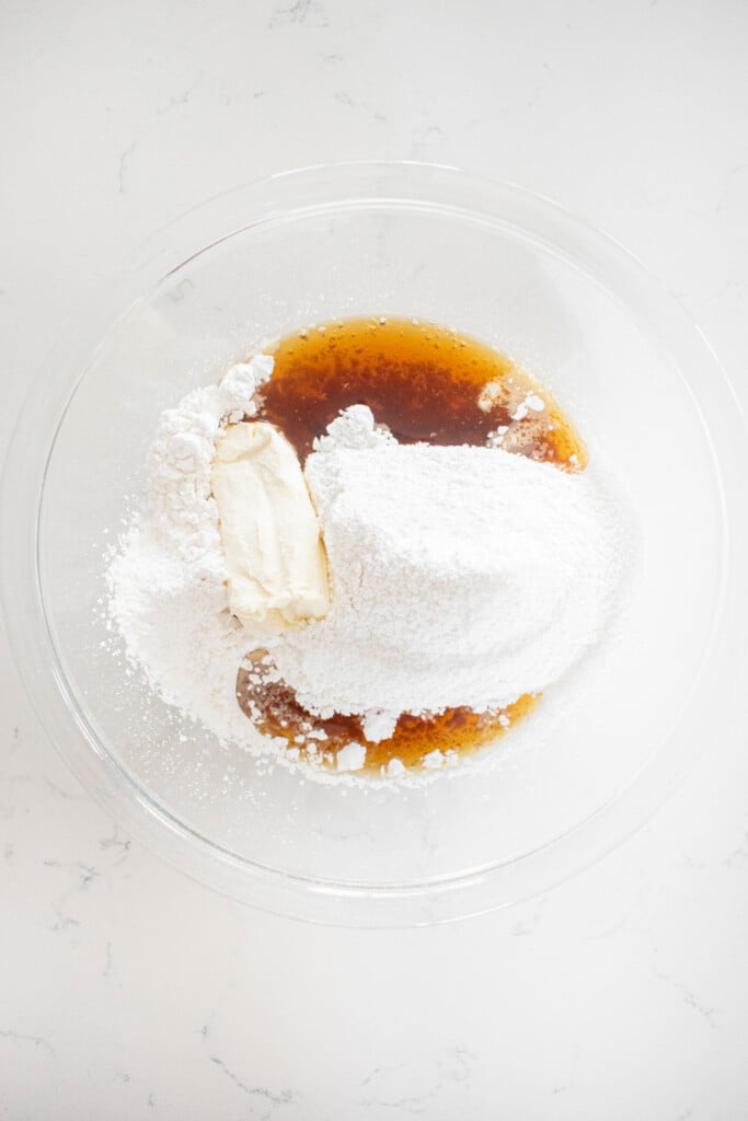 ingredients for maple cream cheese icing in a glass mixing bowl on a white marble counter.