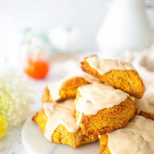 eggless pumpkin spice scones on a marble platter with pumpkins and fresh flowers.
