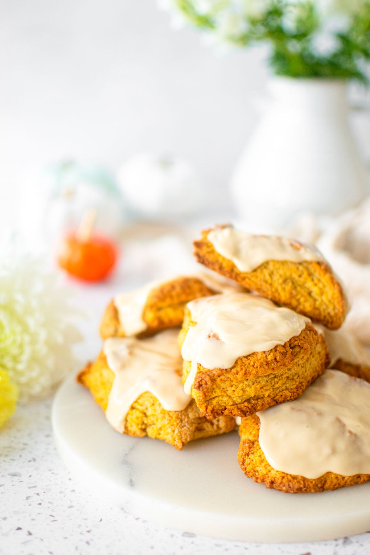 eggless pumpkin spice scones on a marble platter with pumpkins and fresh flowers.