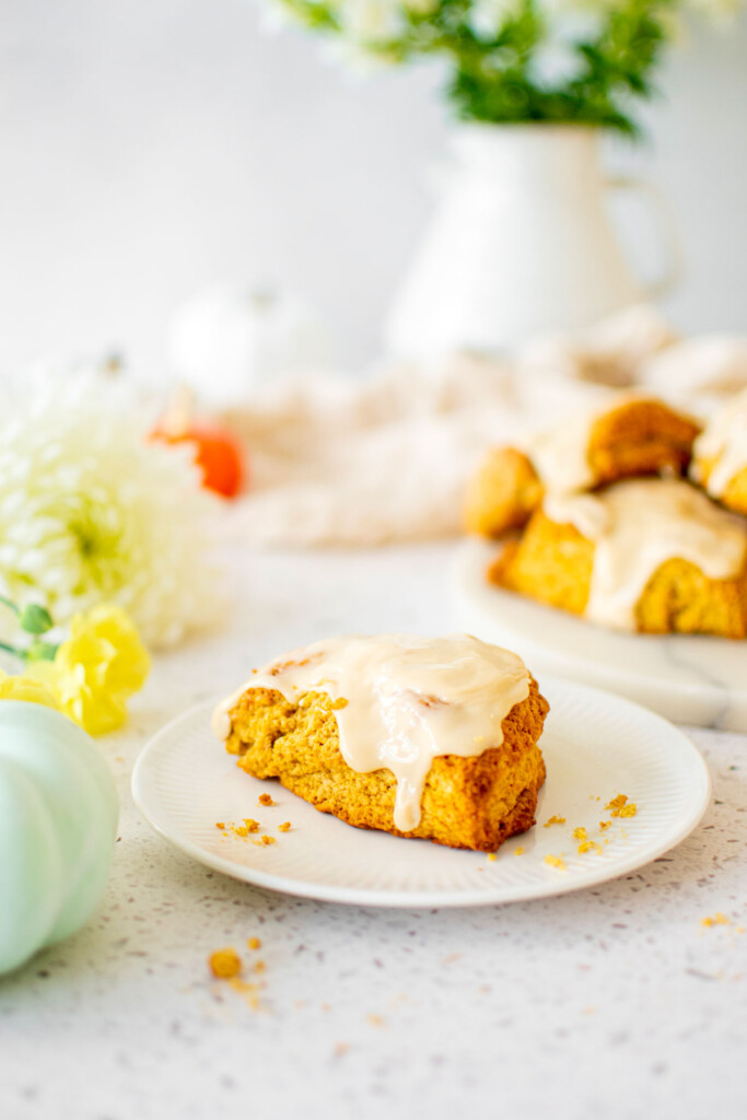 eggless pumpkin spice scone on a plate on a white stone counter with pumpkins.