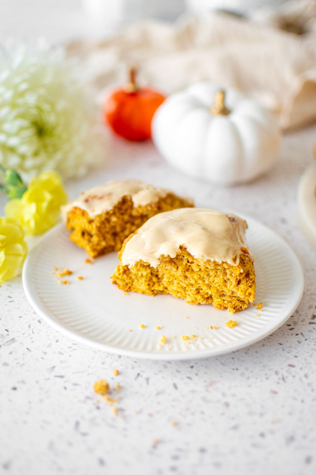 eggless pumpkin spice scone broke in half on a plate on a white stone counter with pumpkins.