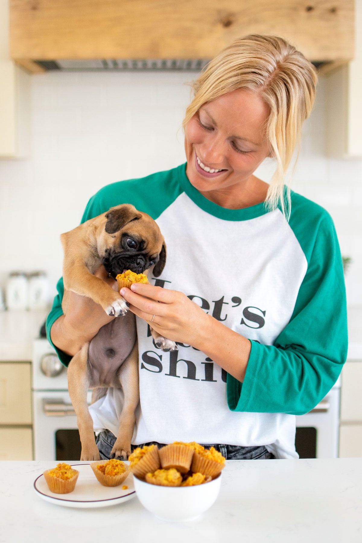woman feeing pug puppy dog muffins at the kitchen counter.